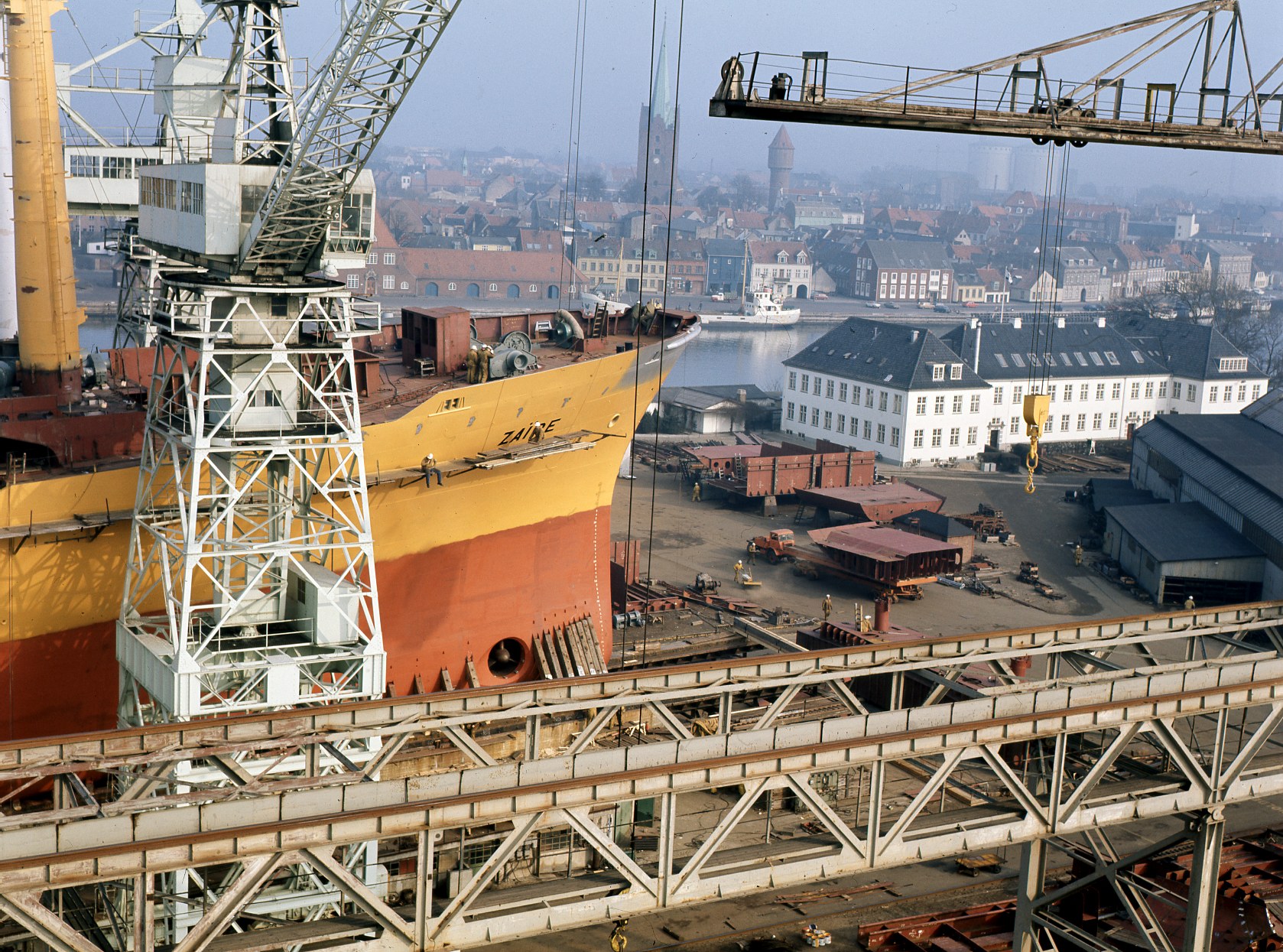 Historisk foto af Nakskov Skibsv&aelig;rft med v&aelig;rftsomr&aring;de, bygninger og skibe ved havnen.